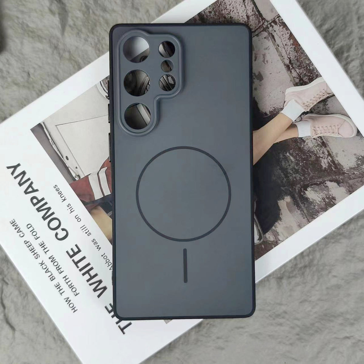 Dark grey case with large MagSafe alignment ring and vertical line detail resting on magazine