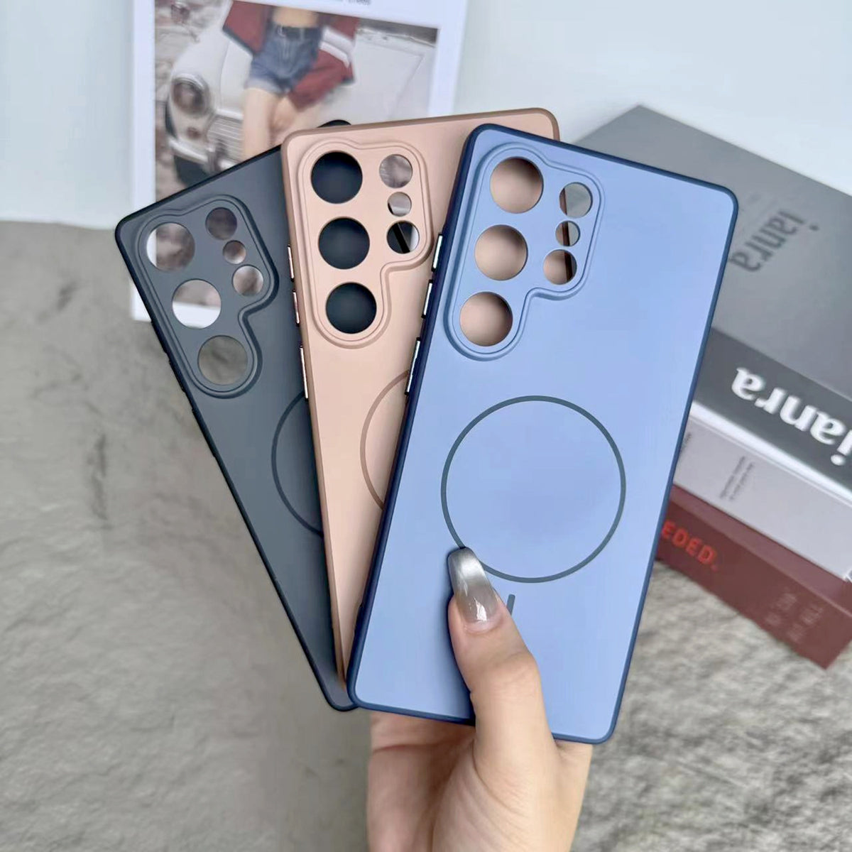 Hand holding dark grey and rose gold cases displaying matte finish against magazine background